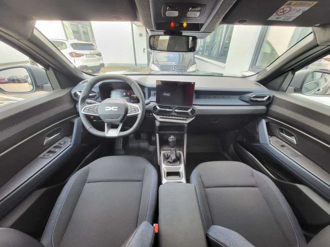 Vue intérieure avant du Dacia Duster TCE 130 4x2 Journey 2025, montrant le tableau de bord moderne et la boîte manuelle.