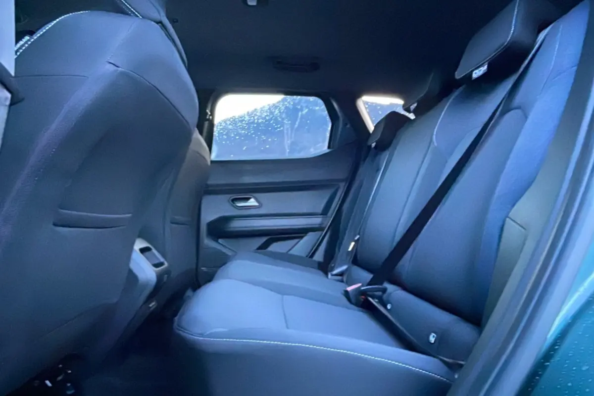 Vue intérieure arrière côté droit du Dacia Duster 2025 vert cèdre, montrant les sièges arrière en tissu sombre.