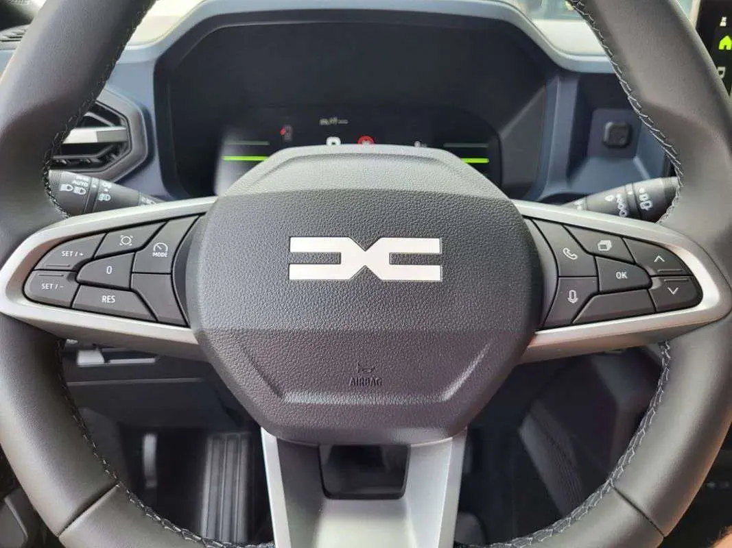 Gros plan sur le volant multifonction du Dacia Duster 2025, avec commandes intégrées et logo central distinctif.