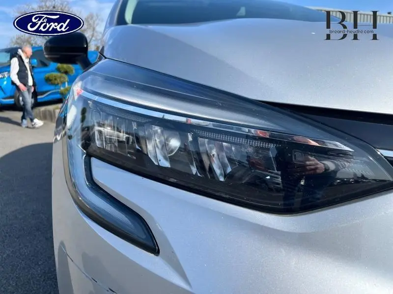 Gros plan sur le phare avant droit gris platine d'une Renault Clio 1.6 E-Tech hybride 2023, avec détails LED visibles.