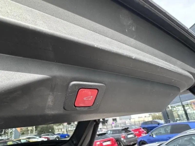 Bouton rouge de fermeture électrique du hayon visible sur le coffre ouvert d’un Peugeot 3008 gris métal 2024.