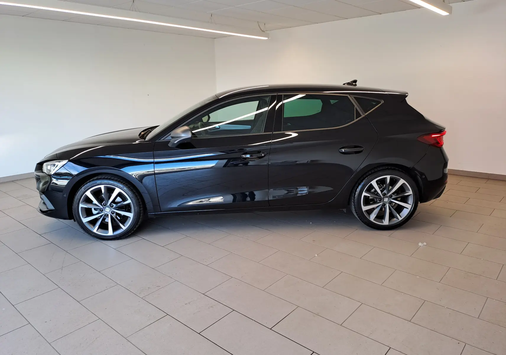 SEAT LEON 1.5 eTSI Hybrid 2024 noir minuit vu de profil côté gauche, jantes alliage et lignes dynamiques.