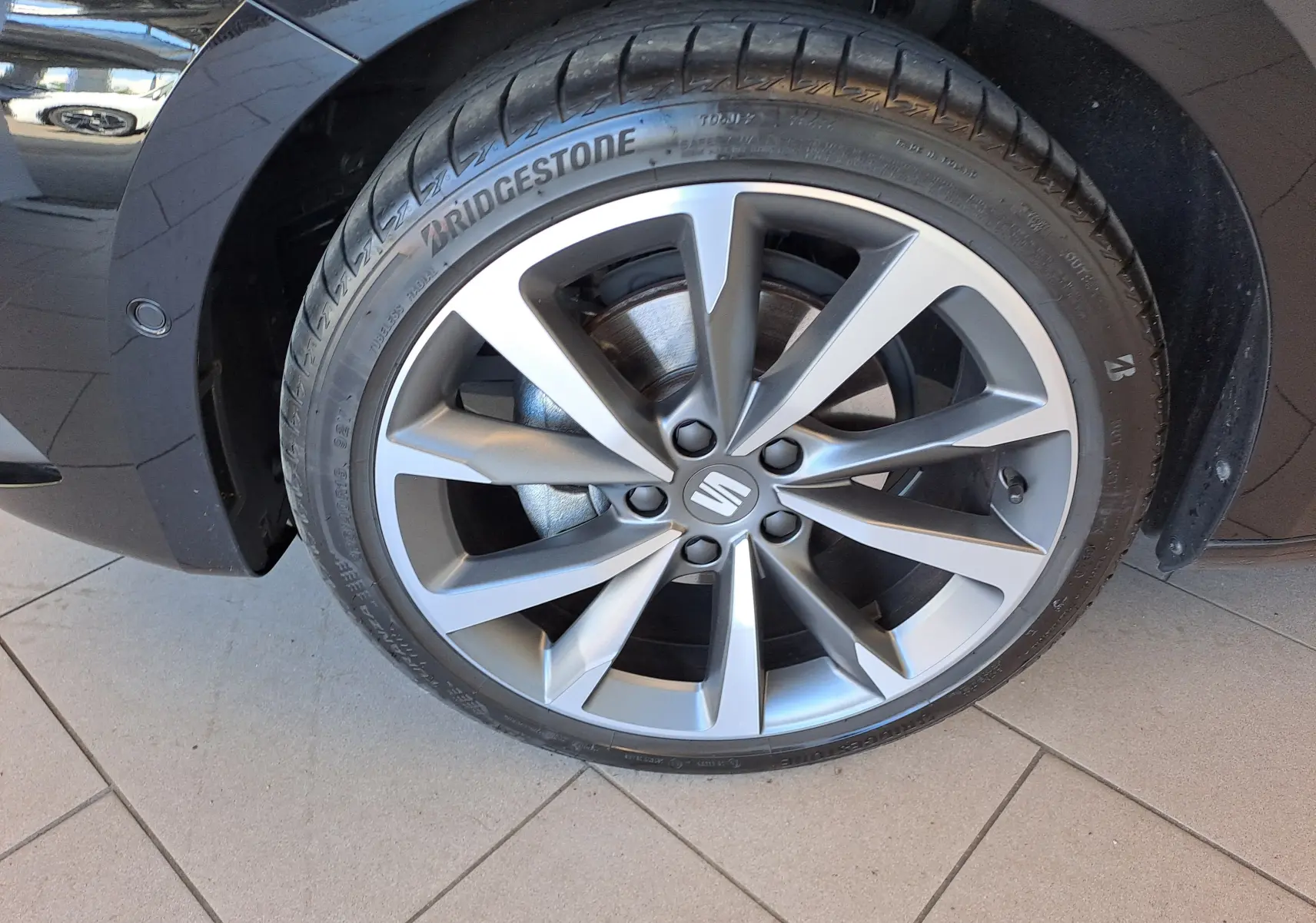 Gros plan sur la roue avant gauche d'une SEAT LEON 1.5 eTSI Hybrid 2024 noir minuit avec jante alliage à 10 branches.