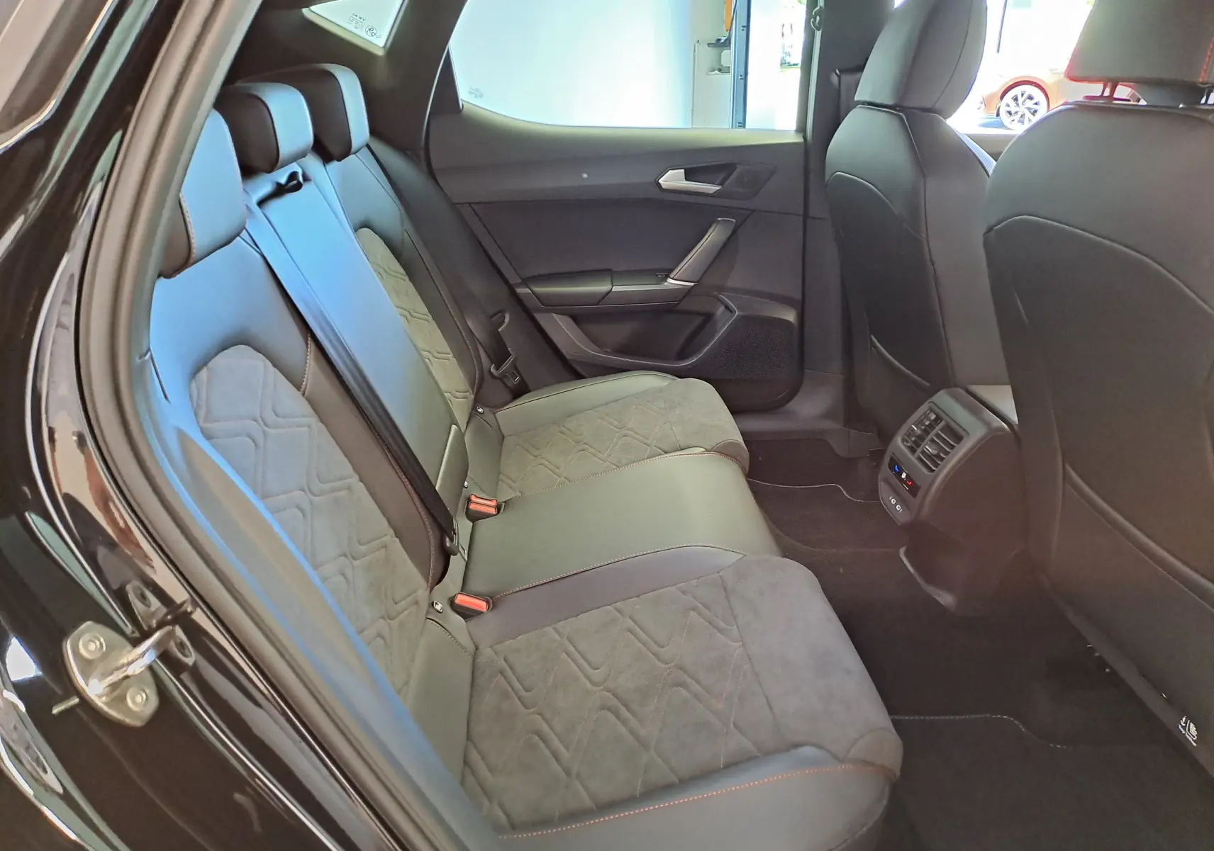 Vue intérieure arrière côté gauche du SEAT LEON 2024 noir minuit, montrant les sièges en tissu et cuir avec surpiqûres orange.