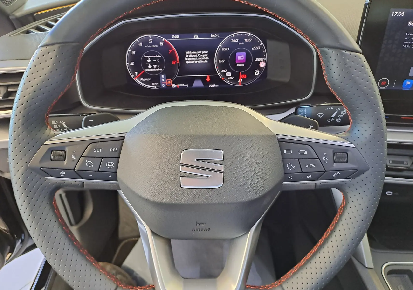 Volant perforé avec surpiqûres rouges de la SEAT LEON 1.5 eTSI Hybrid 2024, tableau de bord numérique visible en arrière-plan.