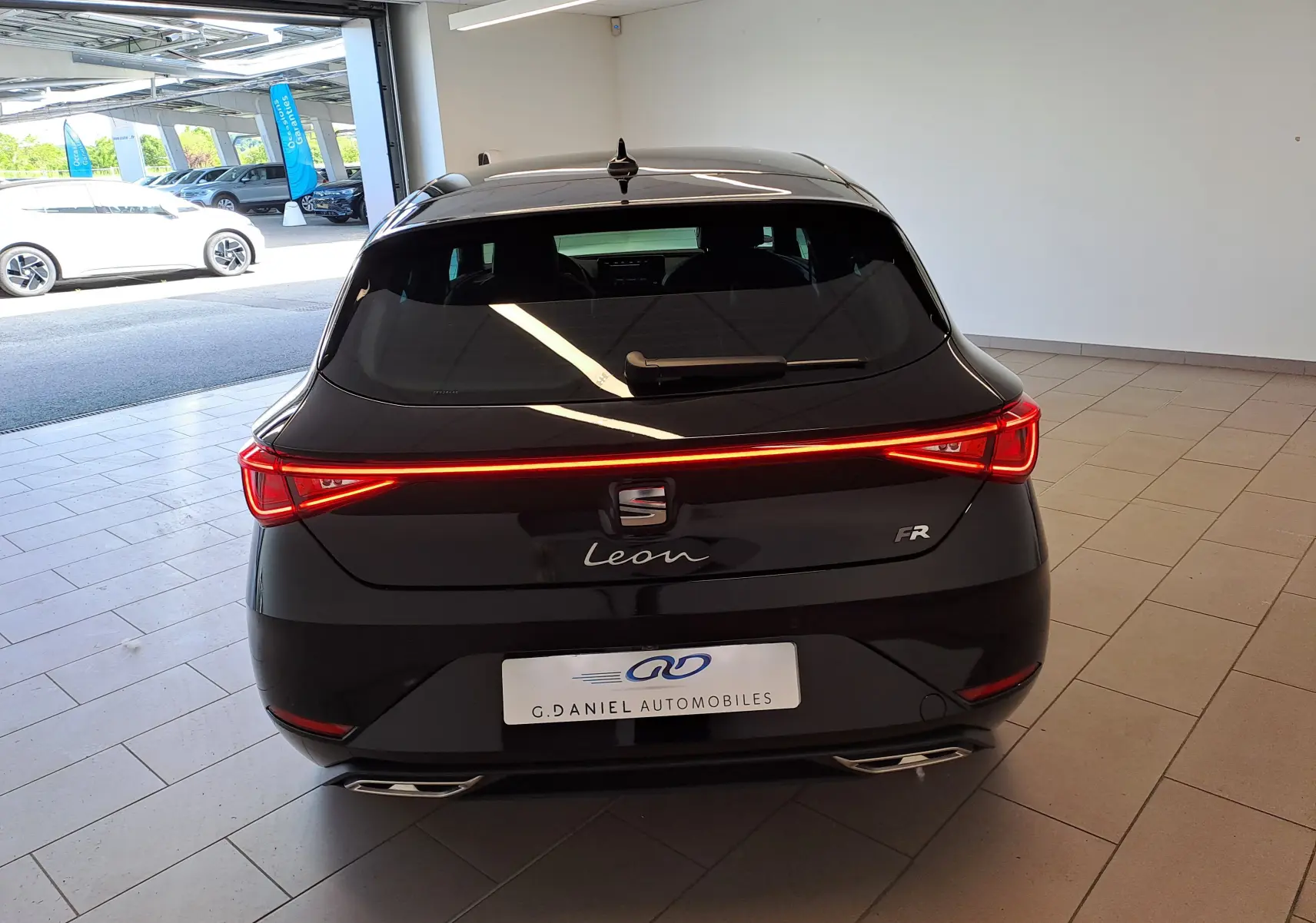 Vue arrière d'une SEAT Leon 1.5 eTSI Hybrid 150 DSG7 FR noire minuit avec feux LED continus allumés en intérieur.