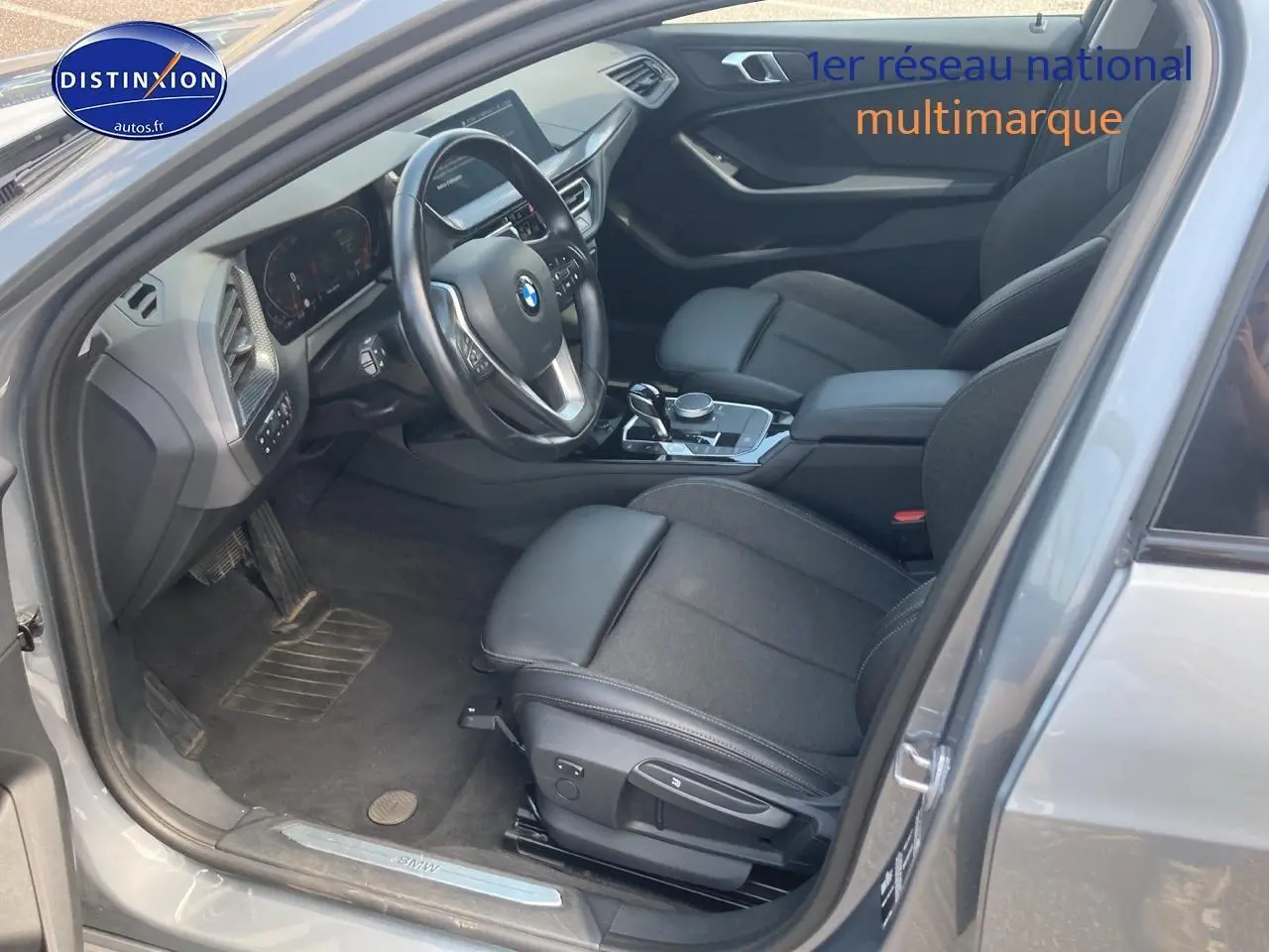 Intérieur côté conducteur d'une BMW Série 1 gris foncé 2023, volant sport cuir et sièges avant sport noirs.