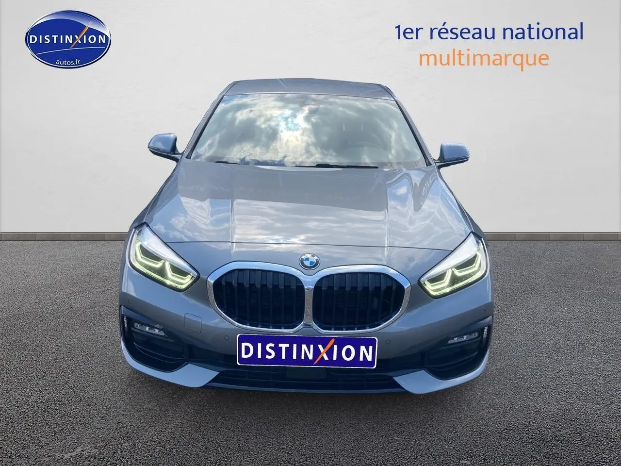 Vue frontale d'une BMW Série 1 gris foncé avec phares LED allumés sur fond neutre.