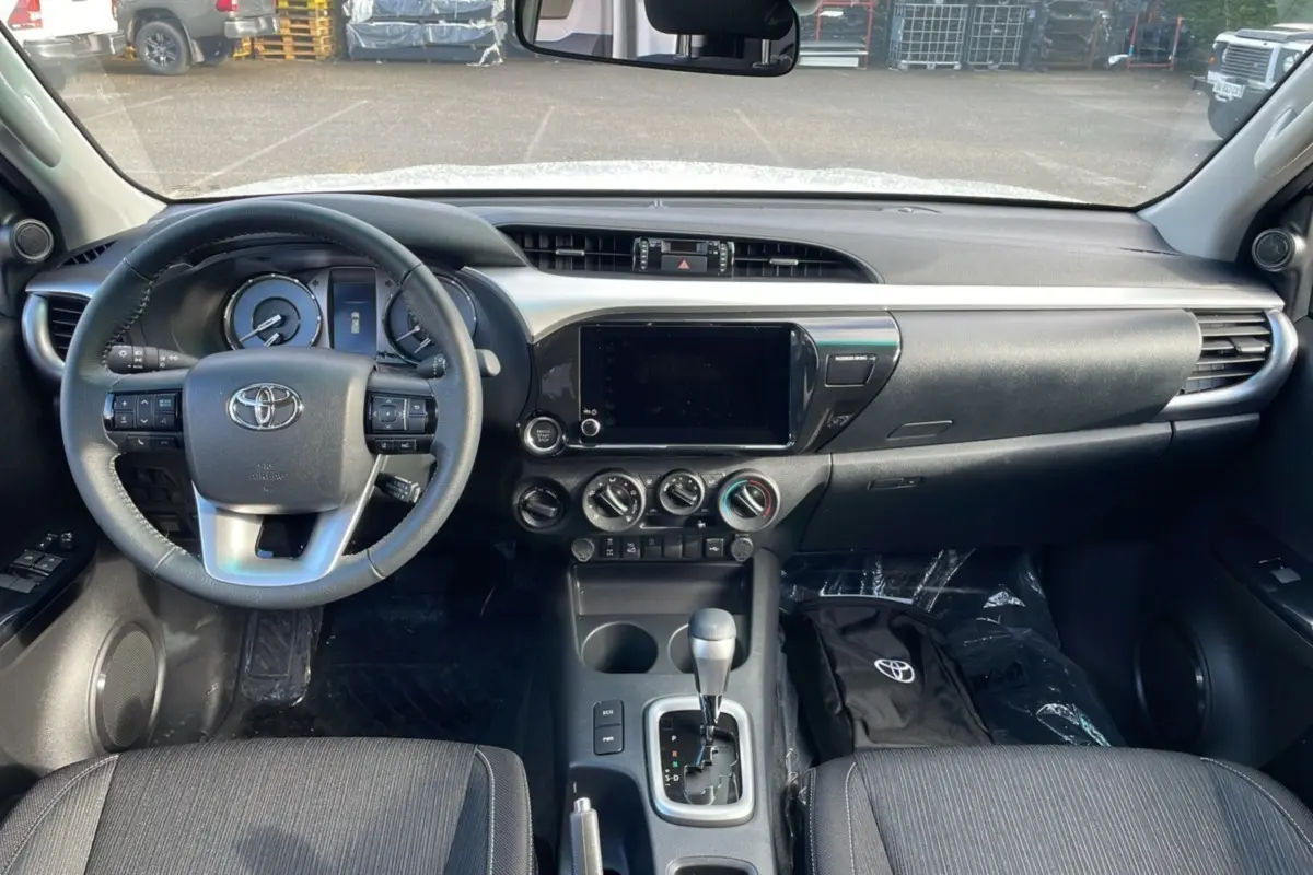 Intérieur du Toyota Hilux 2025 en vue frontale, tableau de bord noir avec écran tactile et levier de boîte automatique.
