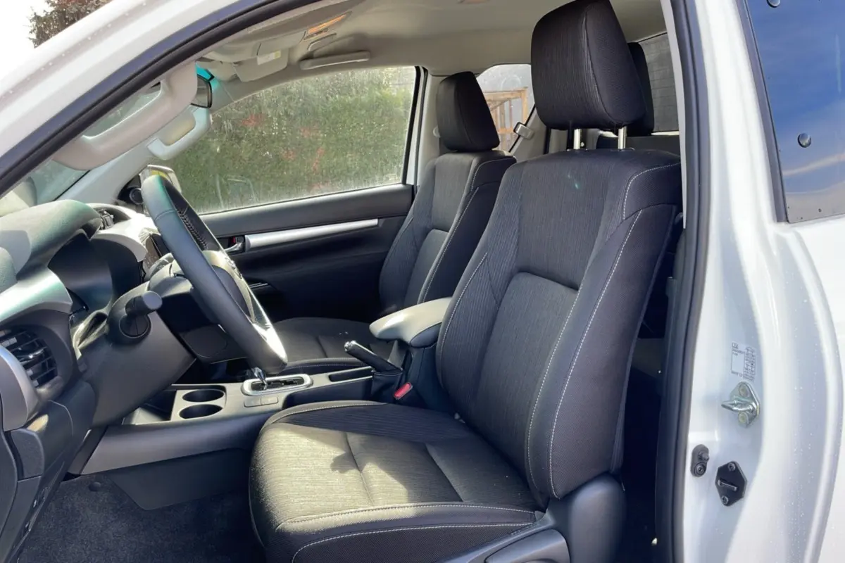 Intérieur du Toyota Hilux 4x4 blanc pur 2025, vue côté conducteur, sièges noirs et tableau de bord visible.