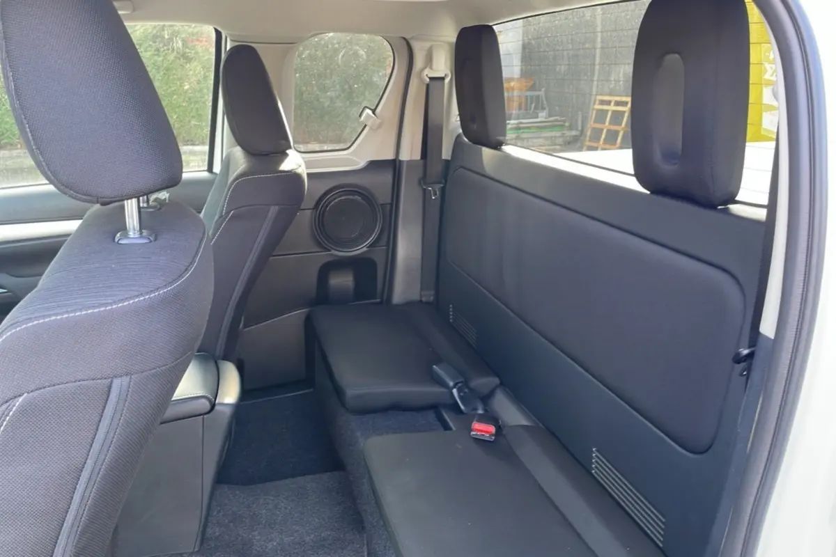 Vue intérieure arrière côté droit du Toyota Hilux 2025 blanc pur, montrant les sièges noirs et un haut-parleur intégré.