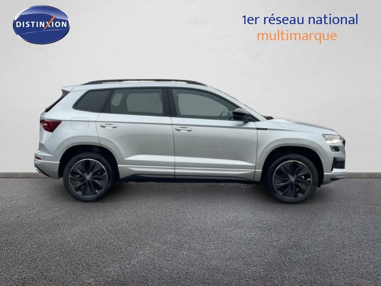 Vue de profil côté gauche d'un Skoda Karoq gris argent métal 2025 avec jantes noires et toit ouvrant.