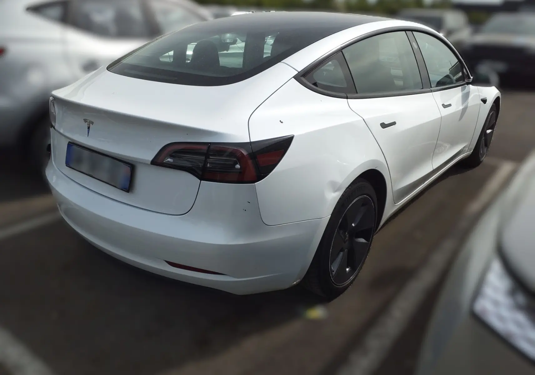 Vue 3/4 arrière droite d'une Tesla Model 3 blanche électrique de 2023, avec jantes noires et toit panoramique.