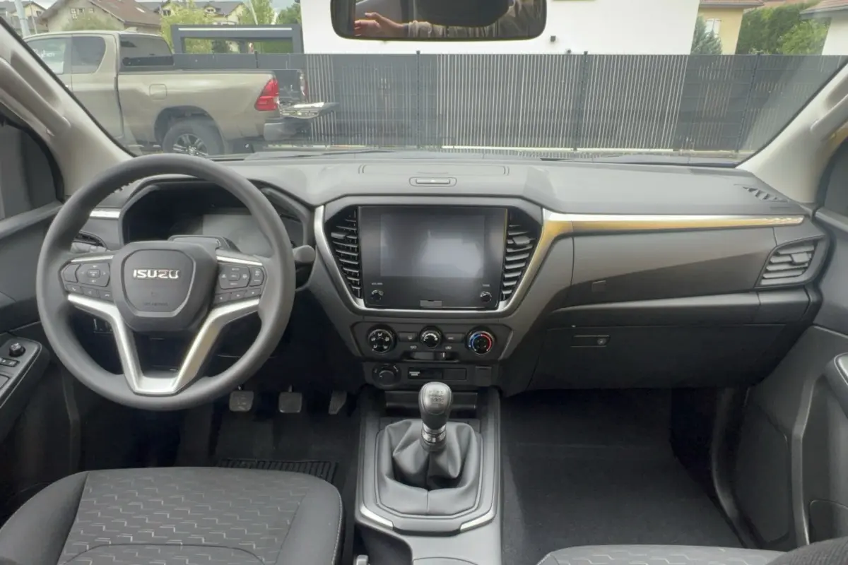 Vue intérieure avant de l'Isuzu D-MAX 2026, tableau de bord noir avec écran tactile et volant multifonctions.