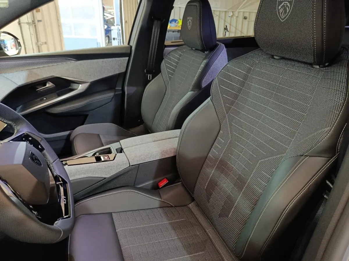 Vue intérieure côté conducteur du Peugeot 5008 1.6 PHEV gris clair, sièges en tissu et cuir avec logo Peugeot brodé sur appuie-tête.