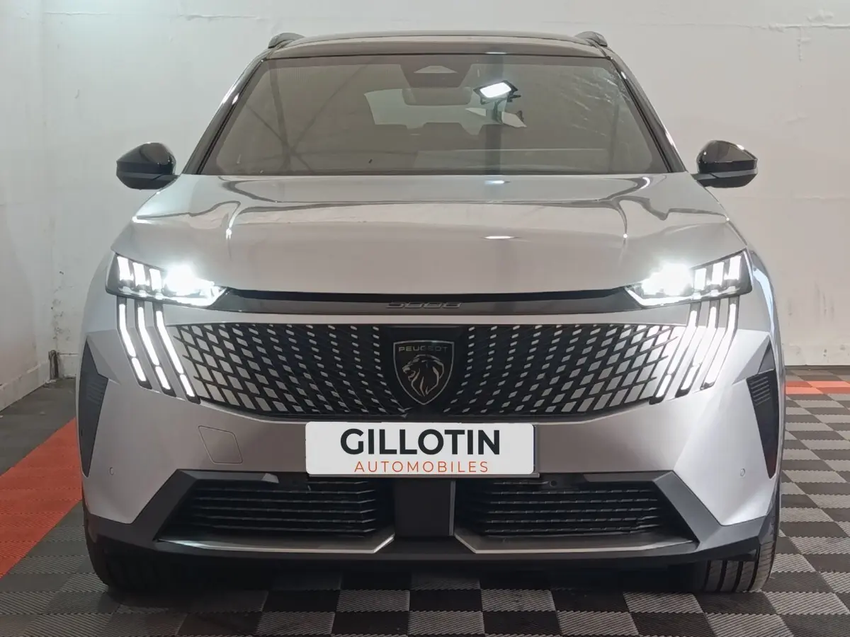 Vue frontale d'un Peugeot 5008 gris clair avec phares LED allumés et calandre distinctive au lion central.