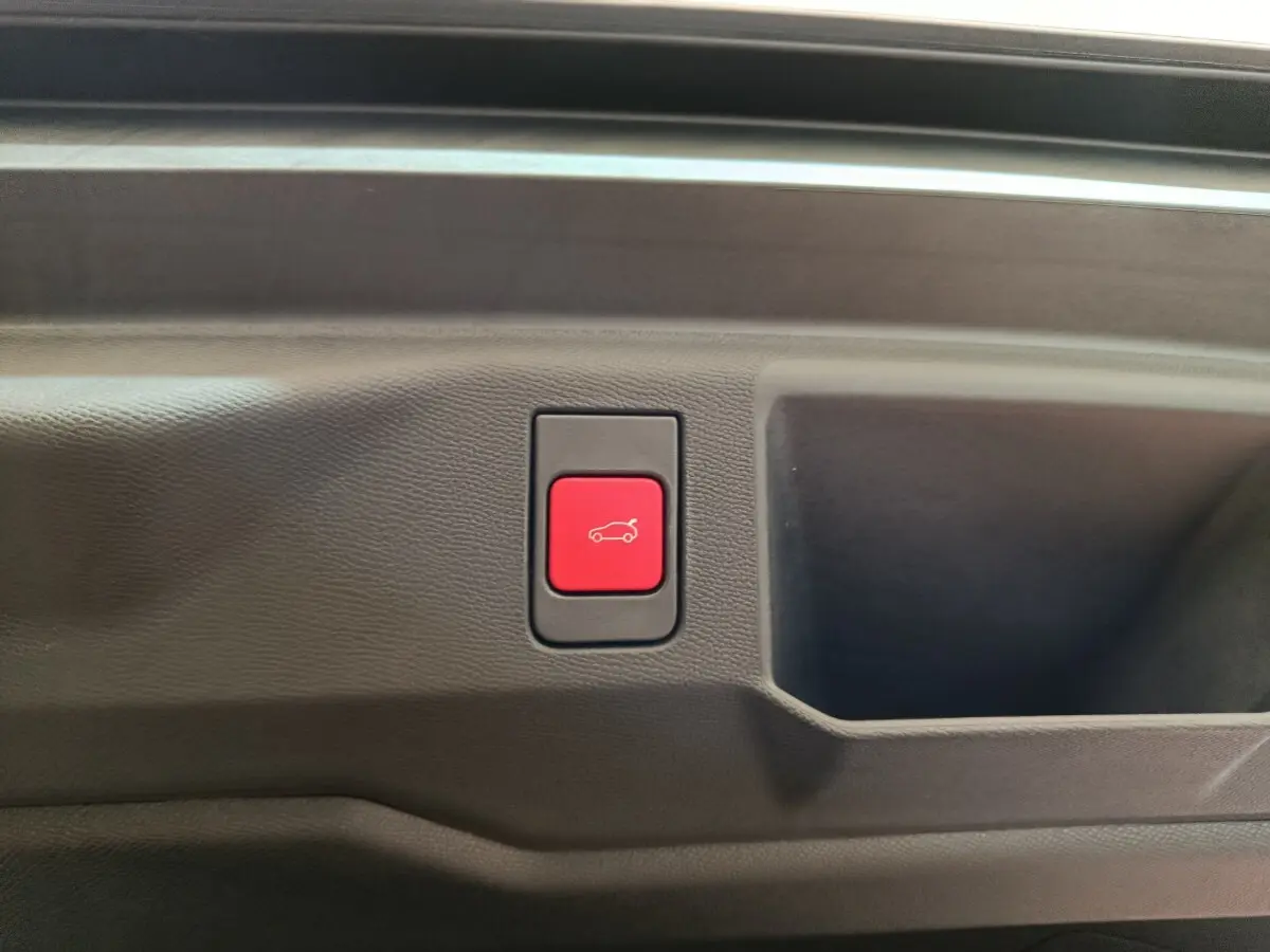 Bouton rouge d'ouverture électrique du coffre sur la garniture intérieure noire d'un Peugeot 5008 gris clair.