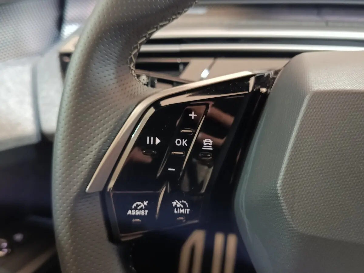Gros plan sur les commandes multifonctions noires à gauche du volant perforé du Peugeot 5008 gris clair 2026.