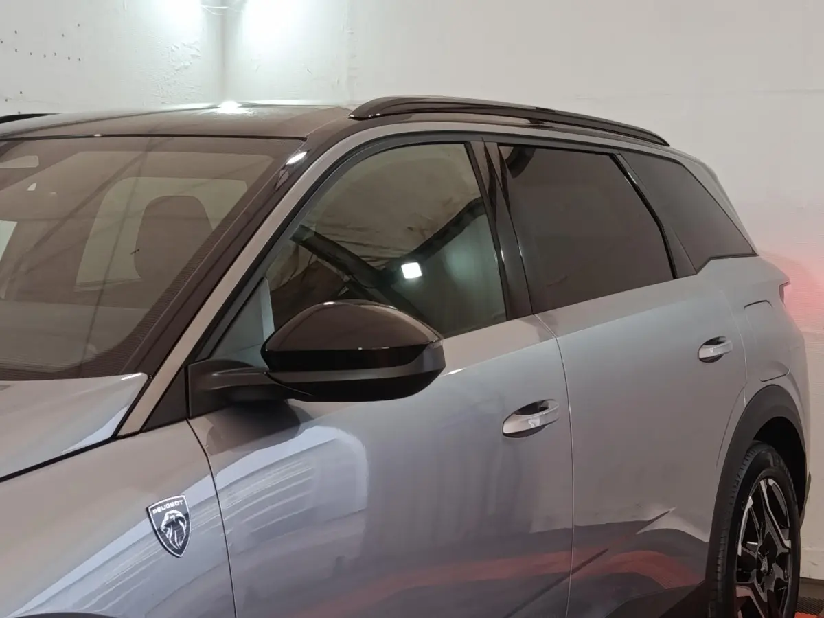 Vue latérale droite du Peugeot 5008 gris clair 2026 avec logo lion et vitres teintées dans un garage.