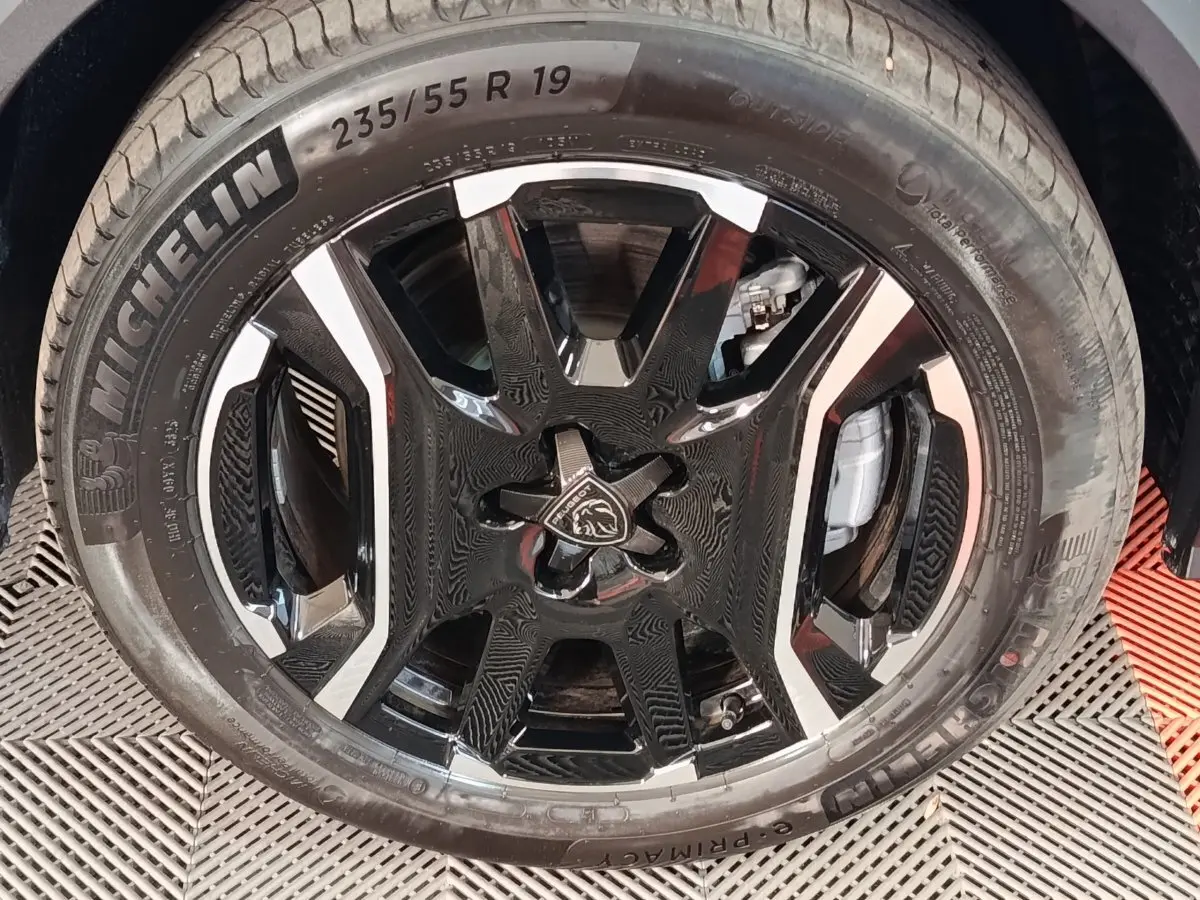 Gros plan sur la jante noire et argentée avec logo Peugeot, montée d’un pneu Michelin 235/55 R19, sur Peugeot 5008 gris clair.