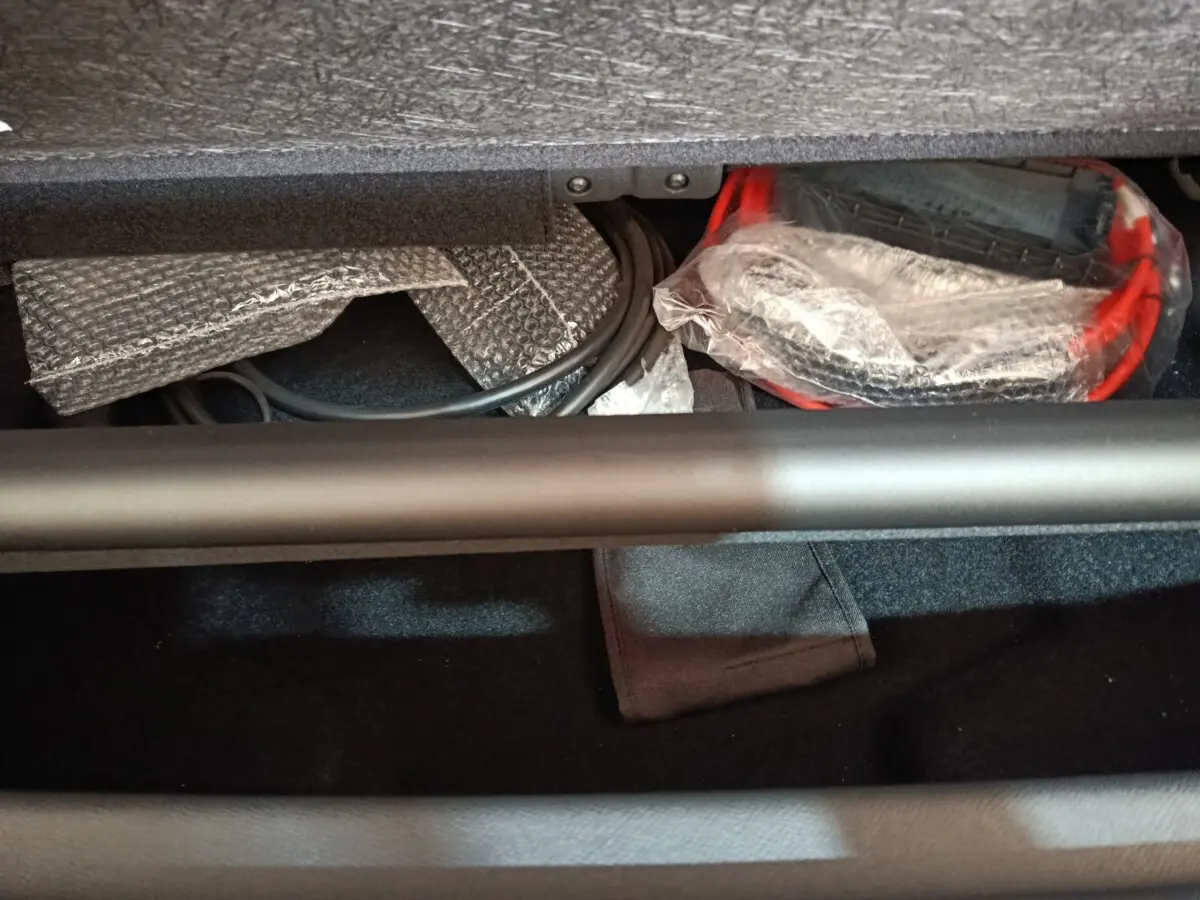 Vue intérieure du coffre du Peugeot 5008 gris clair, montrant câbles et accessoires de recharge rangés sous la tablette.