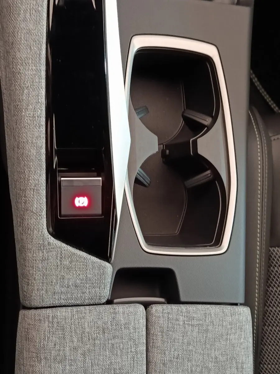 Gros plan sur la console centrale grise du Peugeot 5008 1.6 PHEV avec porte-gobelets et bouton frein à main électrique allumé.