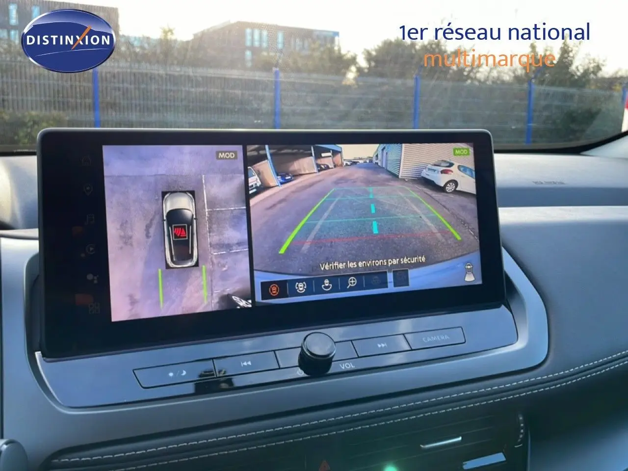 Vue intérieure du tableau de bord du Nissan Qashqai gris argile, affichant l'écran de caméra de recul avec vue 360° et lignes de guidage colorées.