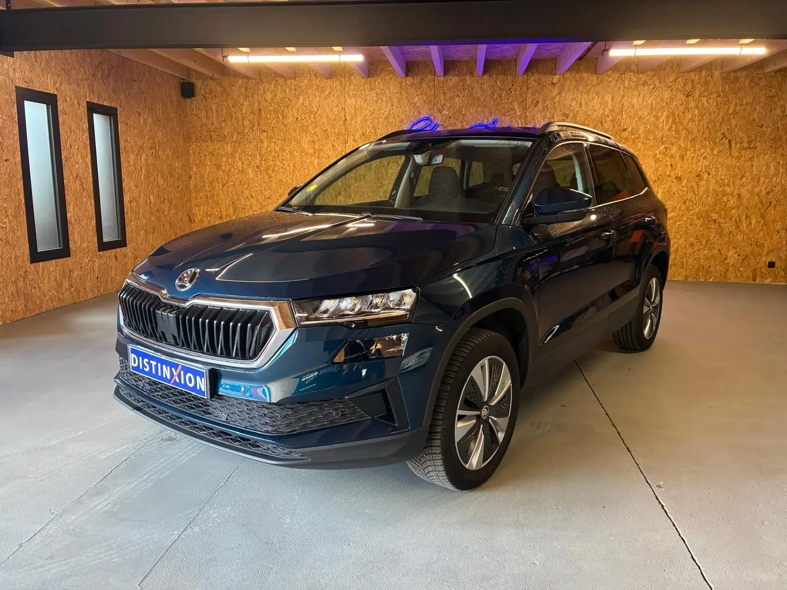 Vue 3/4 avant droite d'un Skoda Karoq bleu 2023 avec calandre chromée et jantes alu 17 pouces en intérieur.