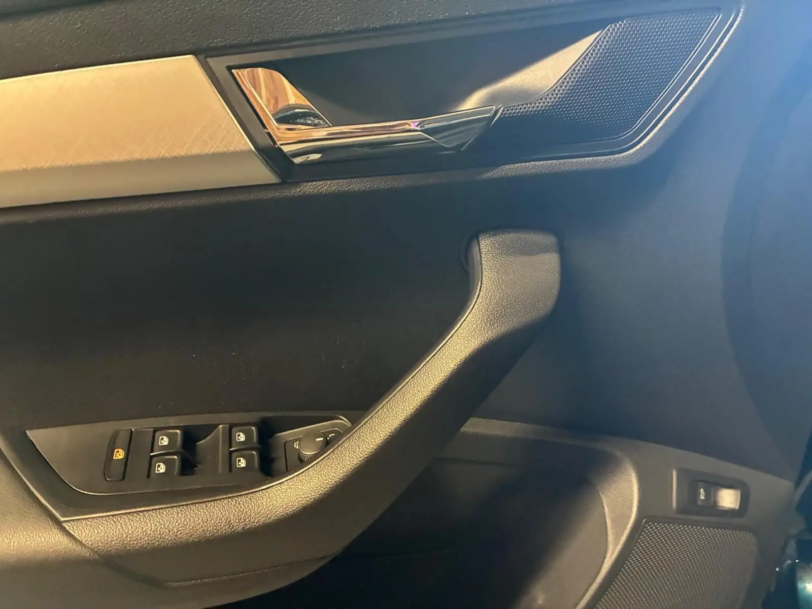 Détail de la porte côté gauche d’un Skoda Karoq bleu 2023 avec commandes de vitres et poignée chromée.