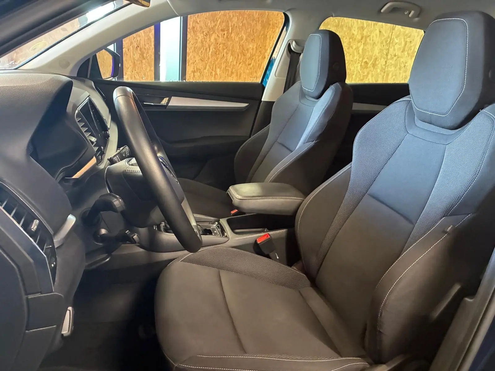 Intérieur avant du Skoda Karoq bleu 2023, sièges tissu gris foncé avec accoudoir central et volant multifonctions.
