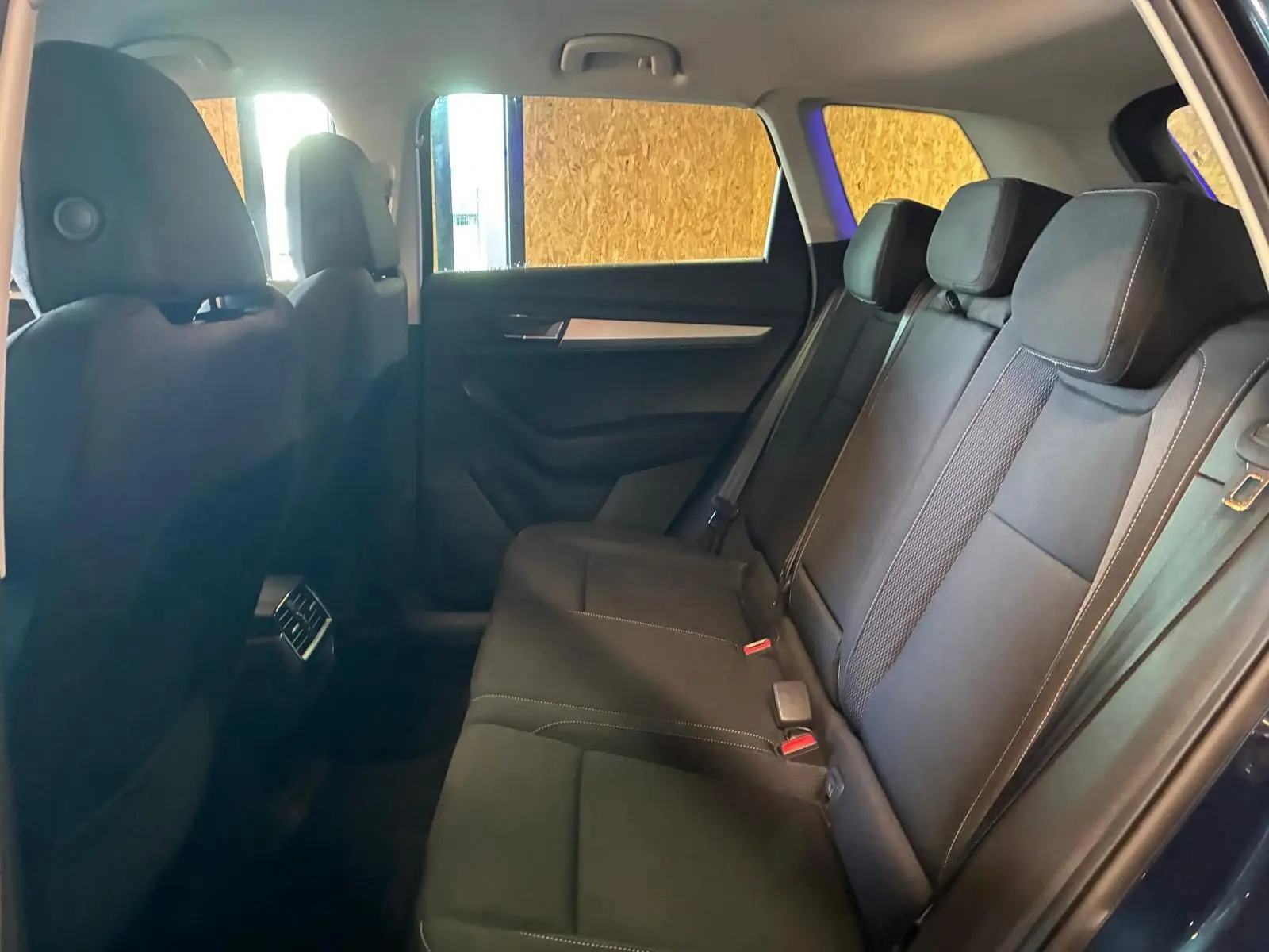 Vue intérieure côté droit des sièges arrière noirs du Skoda Karoq bleu 2023 avec appuie-têtes et ceintures visibles.