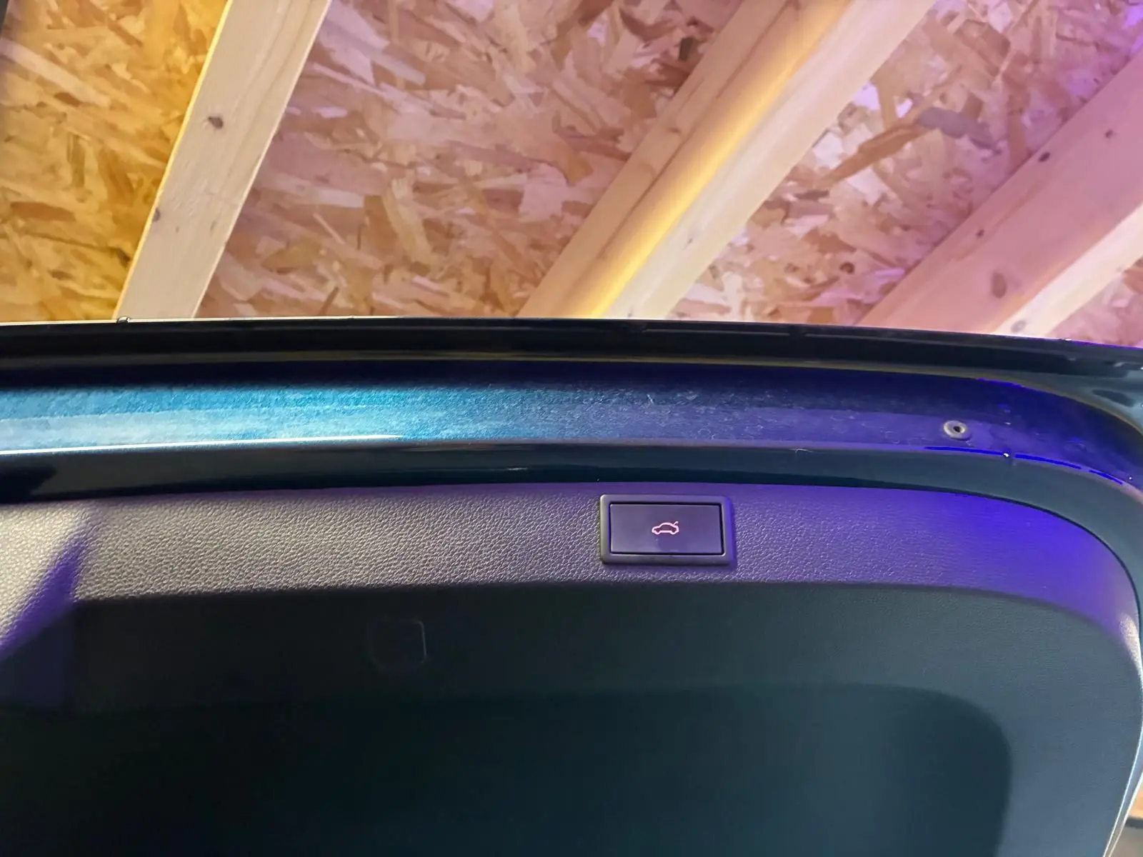 Bouton d'ouverture électrique du hayon sur la face intérieure d'un SKODA KAROQ bleu, vue rapprochée du coffre ouvert.