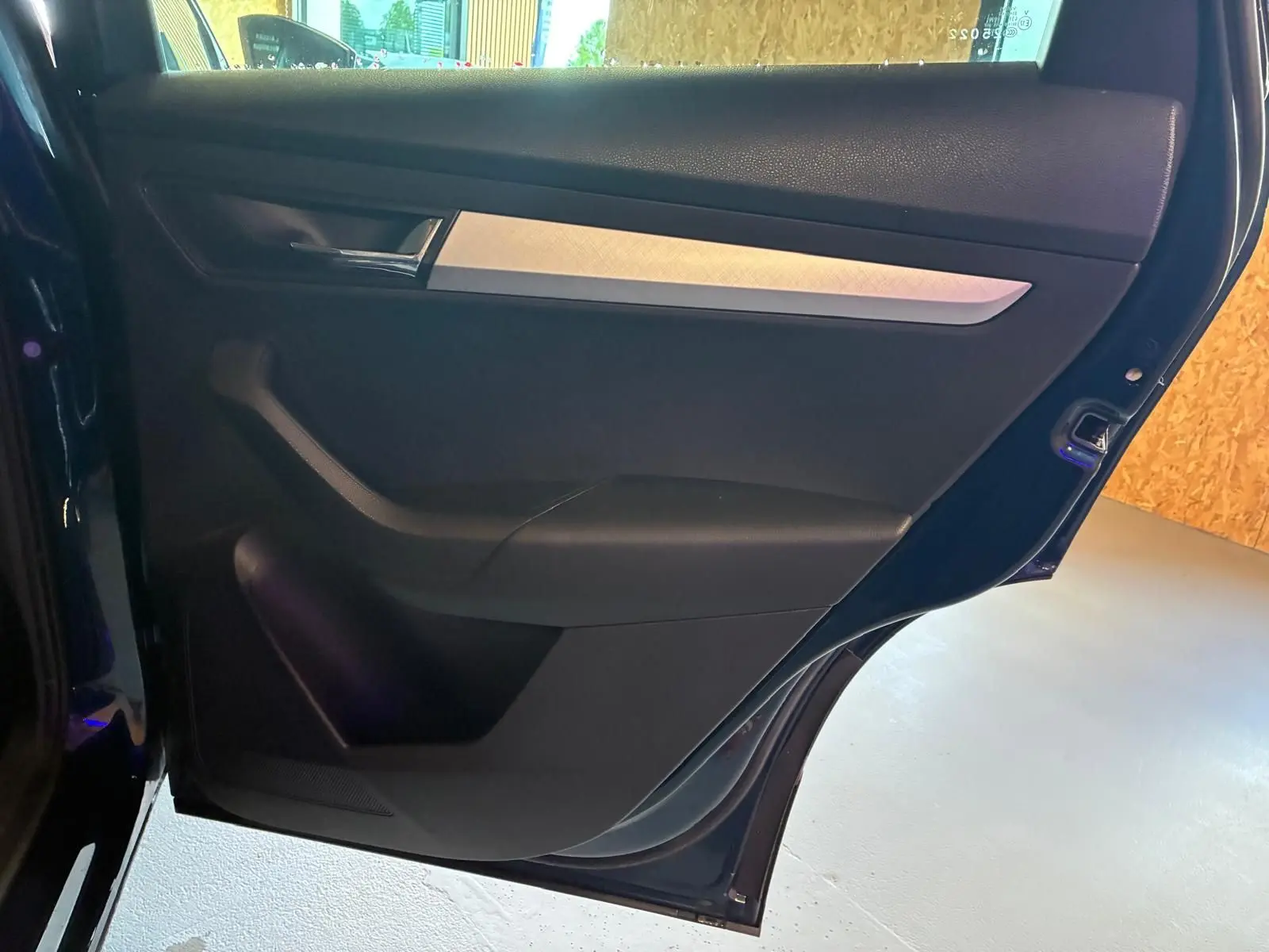 Vue rapprochée de la porte arrière gauche bleu foncé d'un Skoda Karoq 2023 avec insert décoratif gris et poignée chromée.