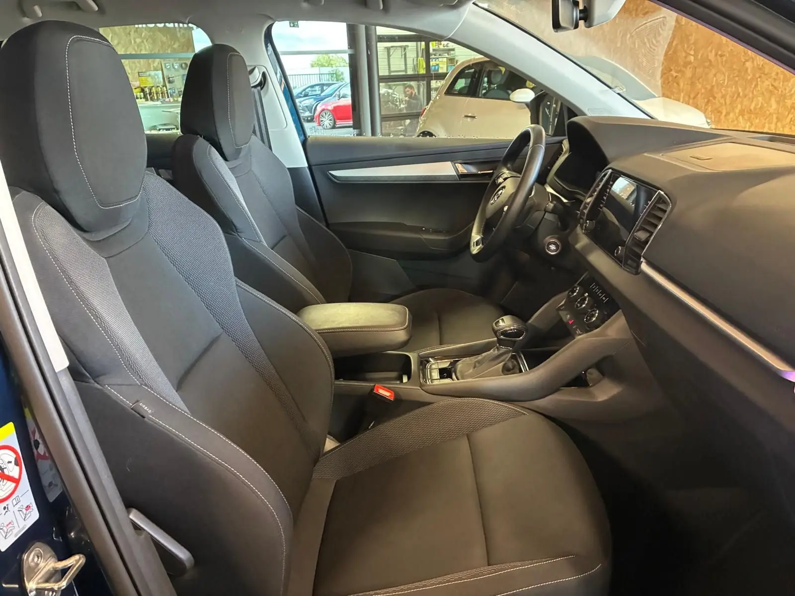 Vue intérieure côté gauche du Skoda Karoq bleu 2023, montrant les sièges avant noirs et le tableau de bord.