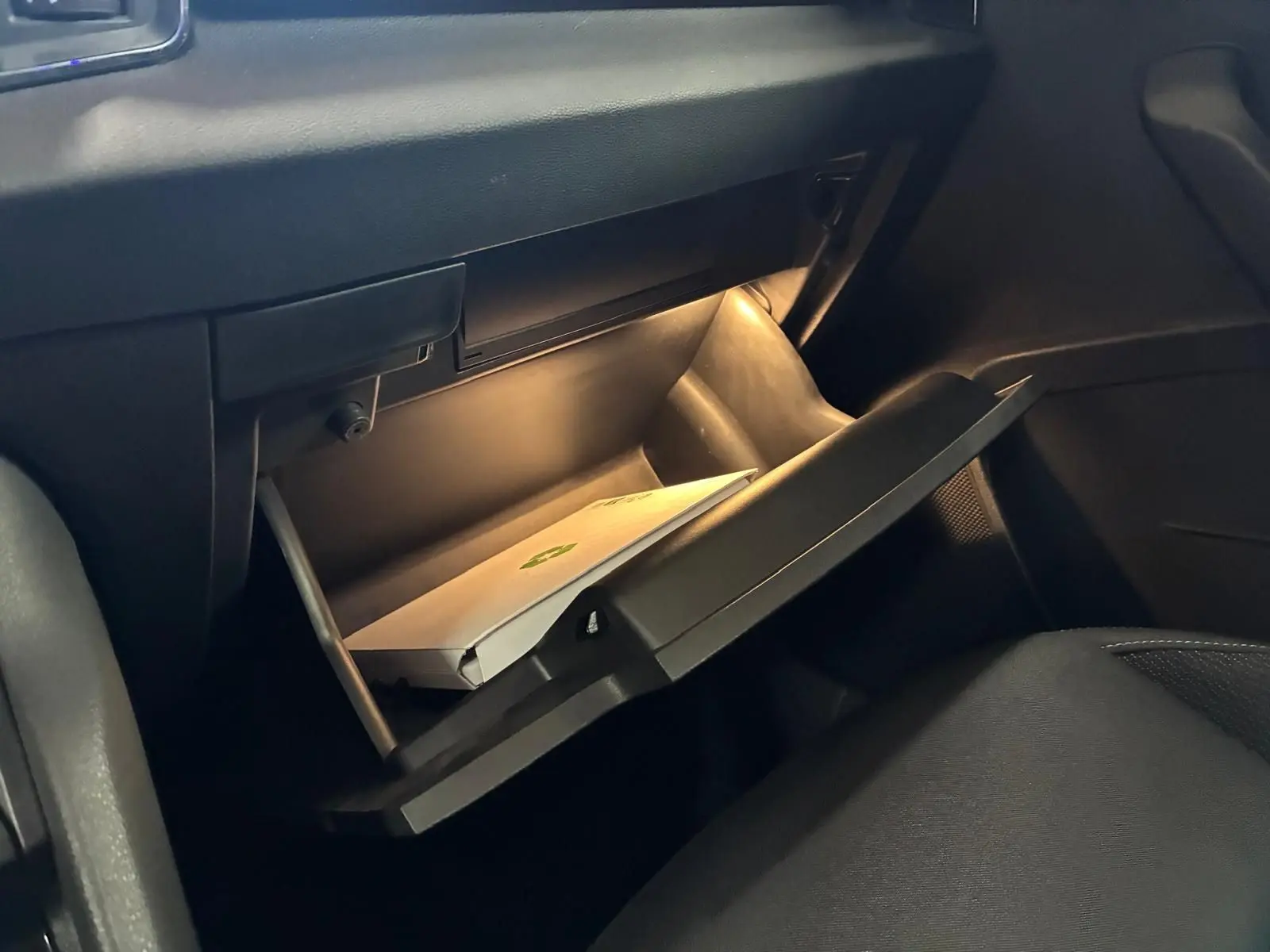 Intérieur de la Skoda Karoq 2023, boîte à gants ouverte avec éclairage intérieur et document visible.