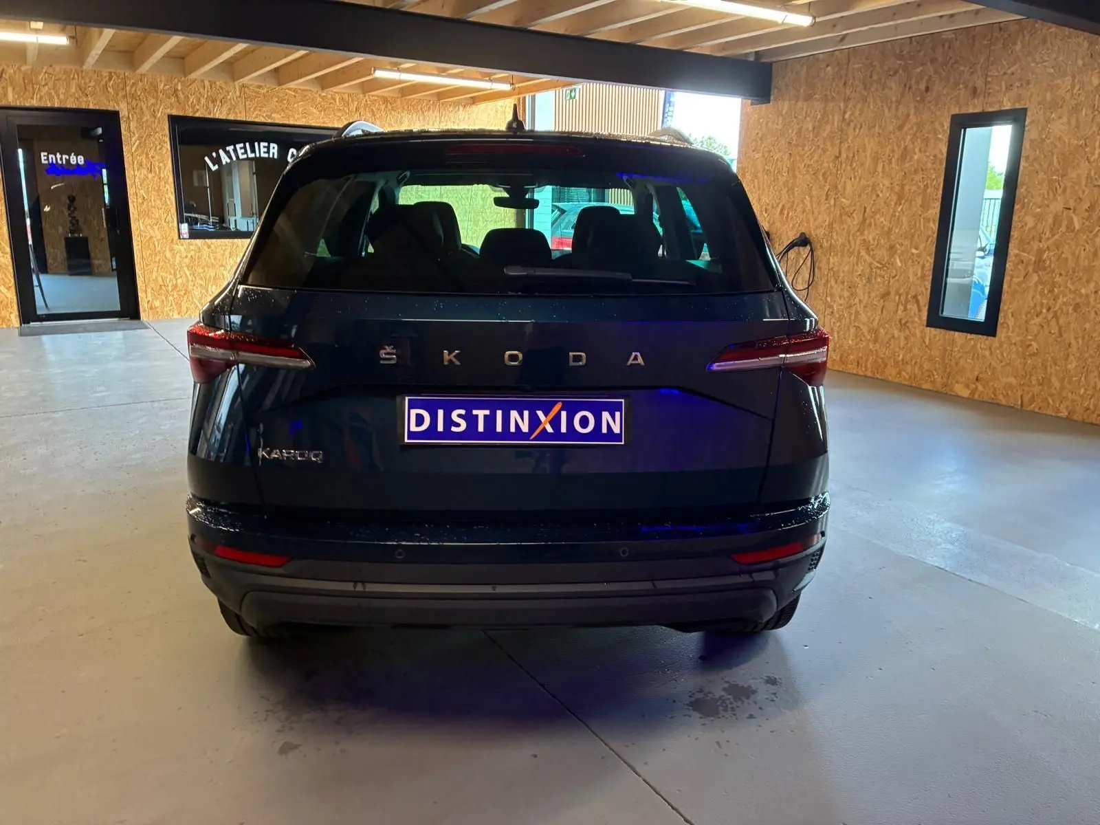 Vue arrière d'un Skoda Karoq bleu 2023 avec feux LED et logo ŠKODA visible en intérieur d'atelier.