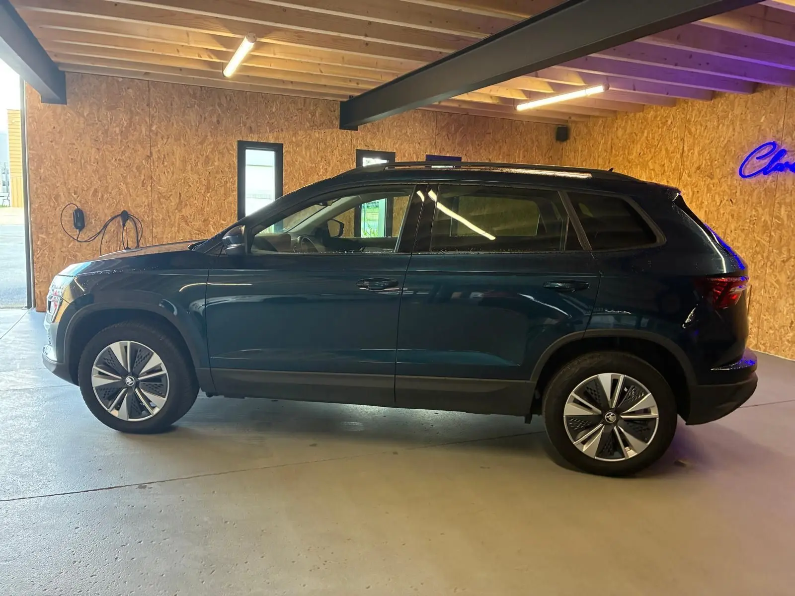 Vue de profil côté gauche d'un SKODA KAROQ bleu 2023 avec jantes alu 17 pouces dans un garage.