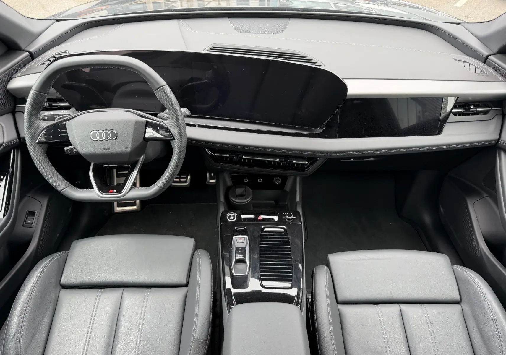 Vue intérieure de face de l’Audi Q6 e-tron 2024 avec tableau de bord noir, volant sport et console centrale brillante.