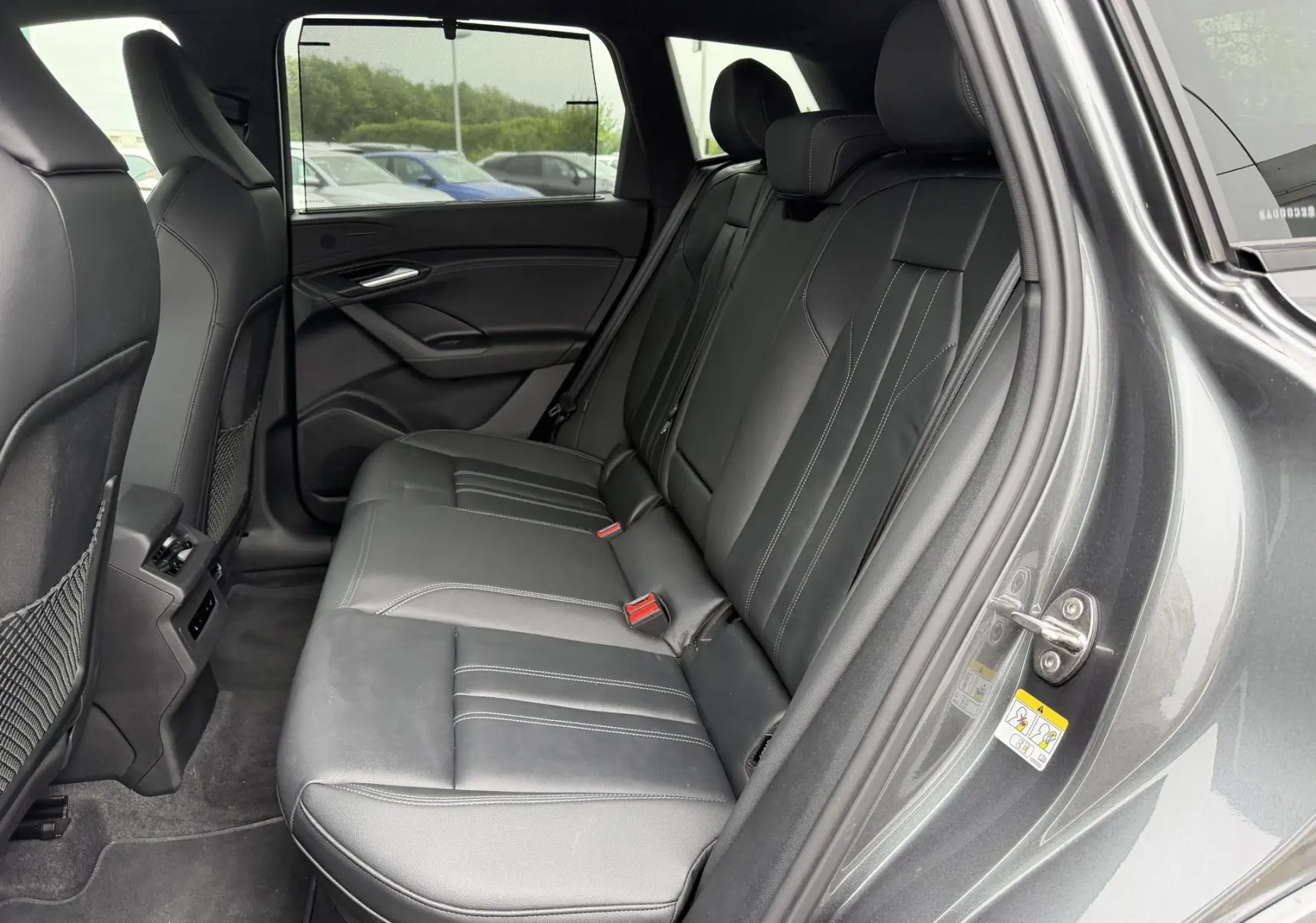 Vue intérieure côté droit des sièges arrière en cuir noir de l'Audi Q6 e-tron gris nacré avec stores pare-soleil manuels.