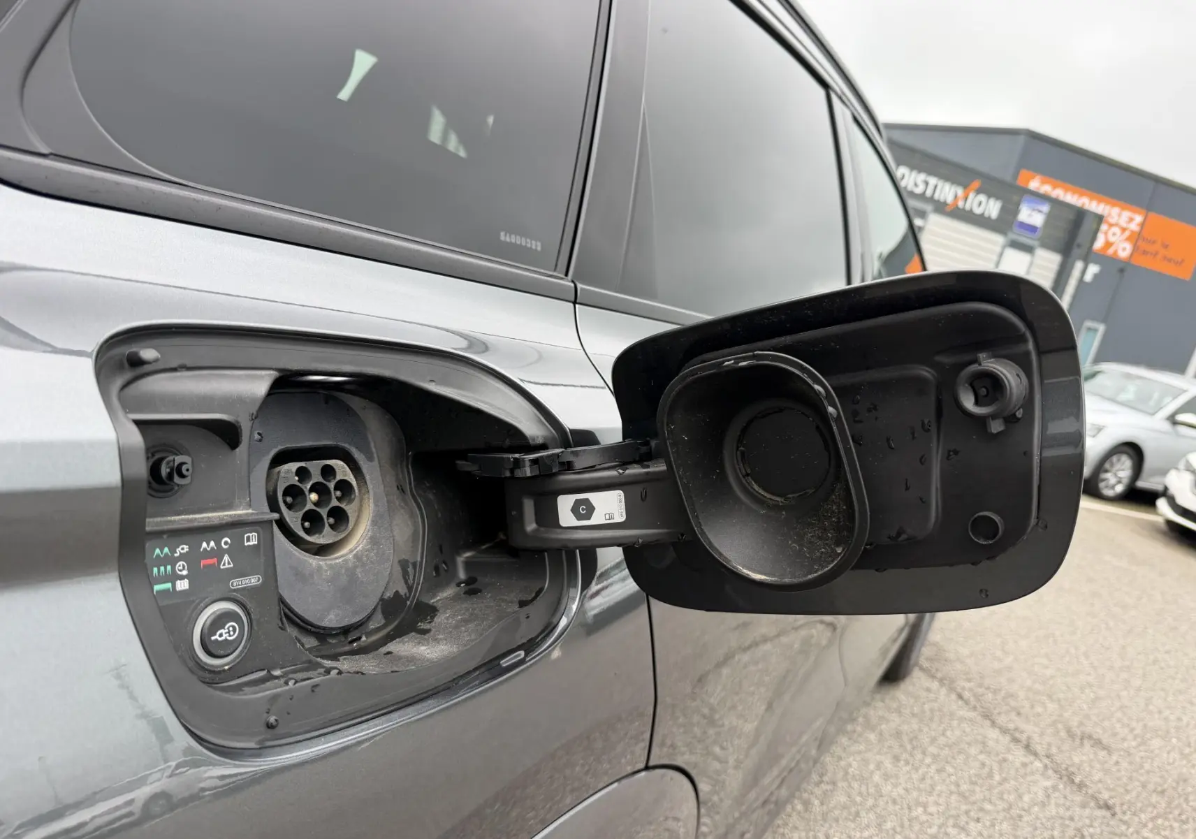 Prise de recharge ouverte côté gauche d’un Audi Q6 e-tron gris nacré, vue rapprochée sur la trappe et la prise électrique.