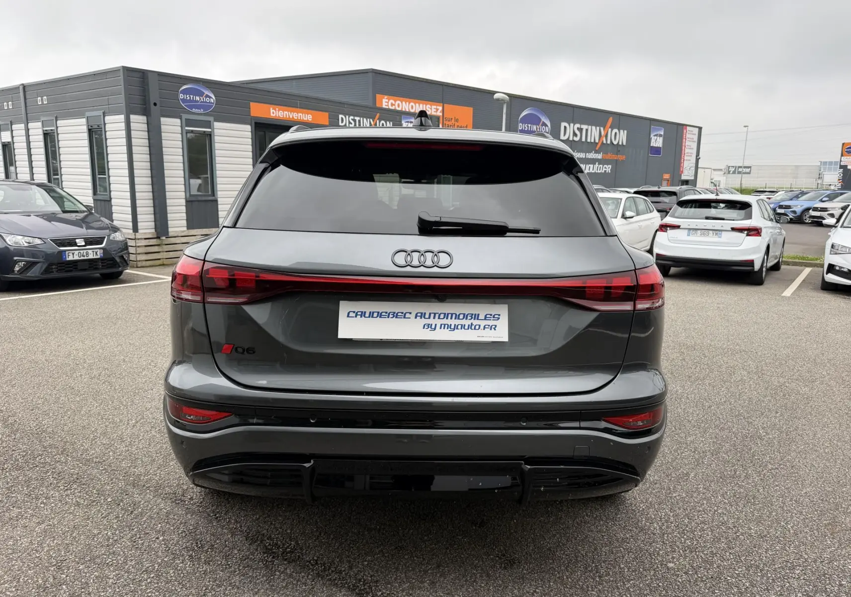 Vue arrière de l'Audi Q6 e-tron gris nacré avec feux arrière reliés et vitres arrière surteintées sur un parking.