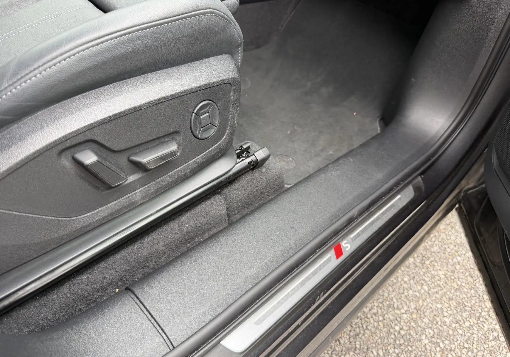 Gros plan sur le seuil de porte avant gauche noir avec logo S et réglages électriques du siège gris.