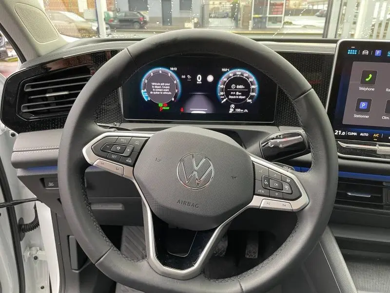 Vue intérieure centrée sur le volant multifonction du Volkswagen Tiguan 2025 avec tableau de bord numérique et écran tactile.