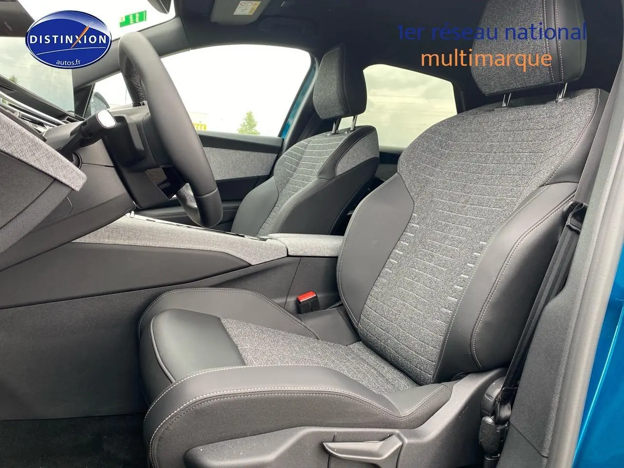 Vue intérieure côté conducteur du Peugeot 3008 bleu 2025, mettant en valeur les sièges tissu et cuir gris avec accoudoir central.