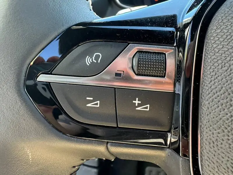 Gros plan sur les commandes au volant côté gauche du Peugeot 2008 hybride 2025, avec boutons de volume et reconnaissance vocale.