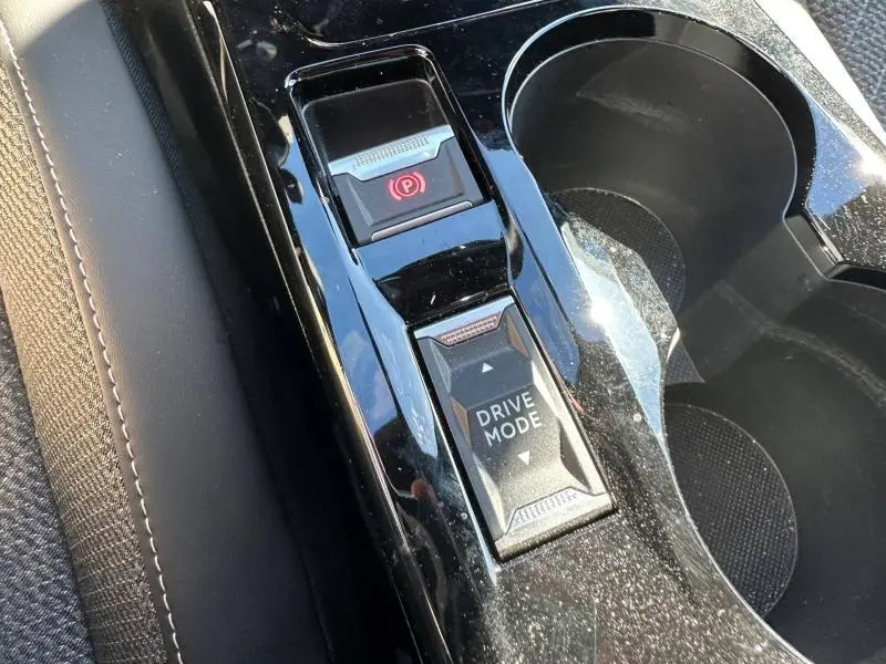 Gros plan sur la console centrale noire brillante du Peugeot 2008 Hybrid 2025, avec bouton Drive Mode et frein à main électronique.