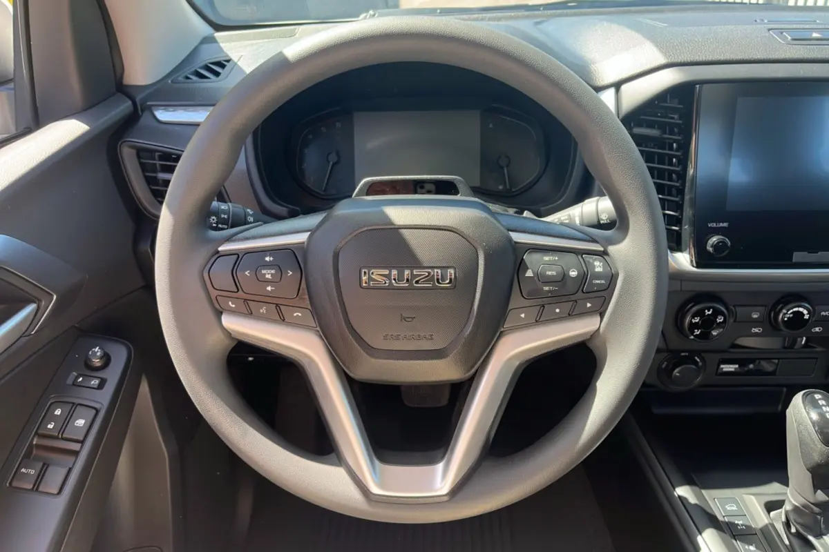 Vue intérieure centrée sur le volant multifonctions ISUZU et tableau de bord du D-MAX 2026, détails des commandes visibles.