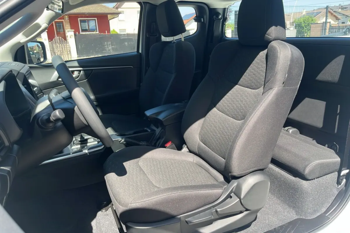 Vue intérieure côté conducteur de l'Isuzu D-MAX 2.2 TD 164 Space Evolution avec sièges tissu gris et accoudoir central.