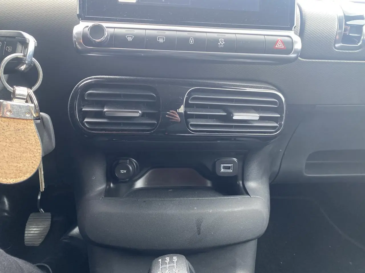 Vue rapprochée de la console centrale noire du Citroën C4 Cactus 2015 avec ventilation, prise 12V et port USB visible.