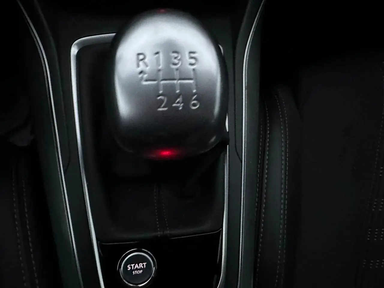 Gros plan sur le levier de vitesses manuel et le bouton start/stop dans l'habitacle noir d'une Peugeot 308.